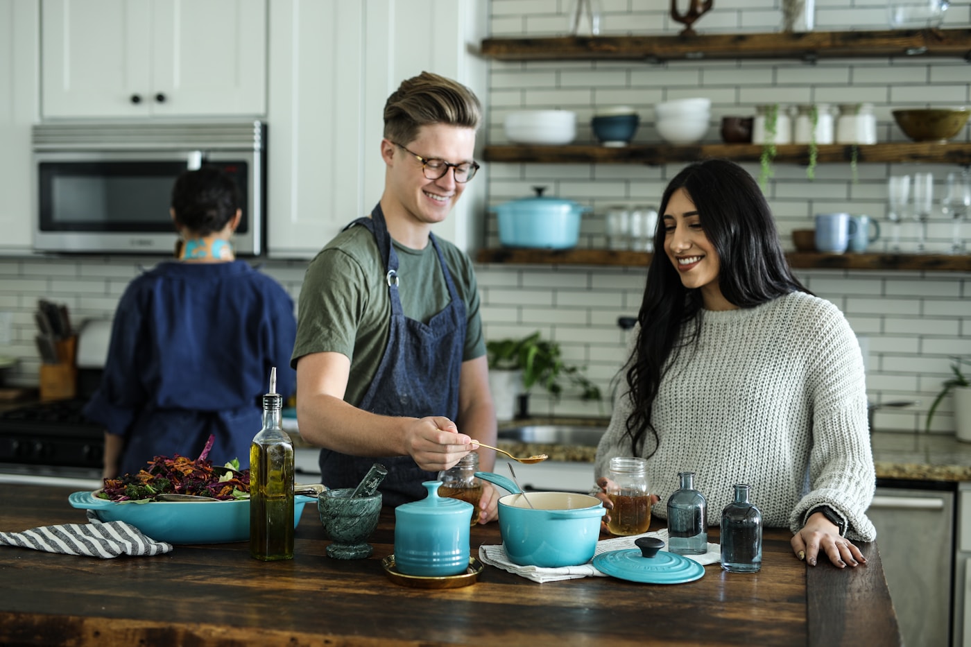 A few neighbors gathered around a kitchen island, cooking and serving food together from a big pot