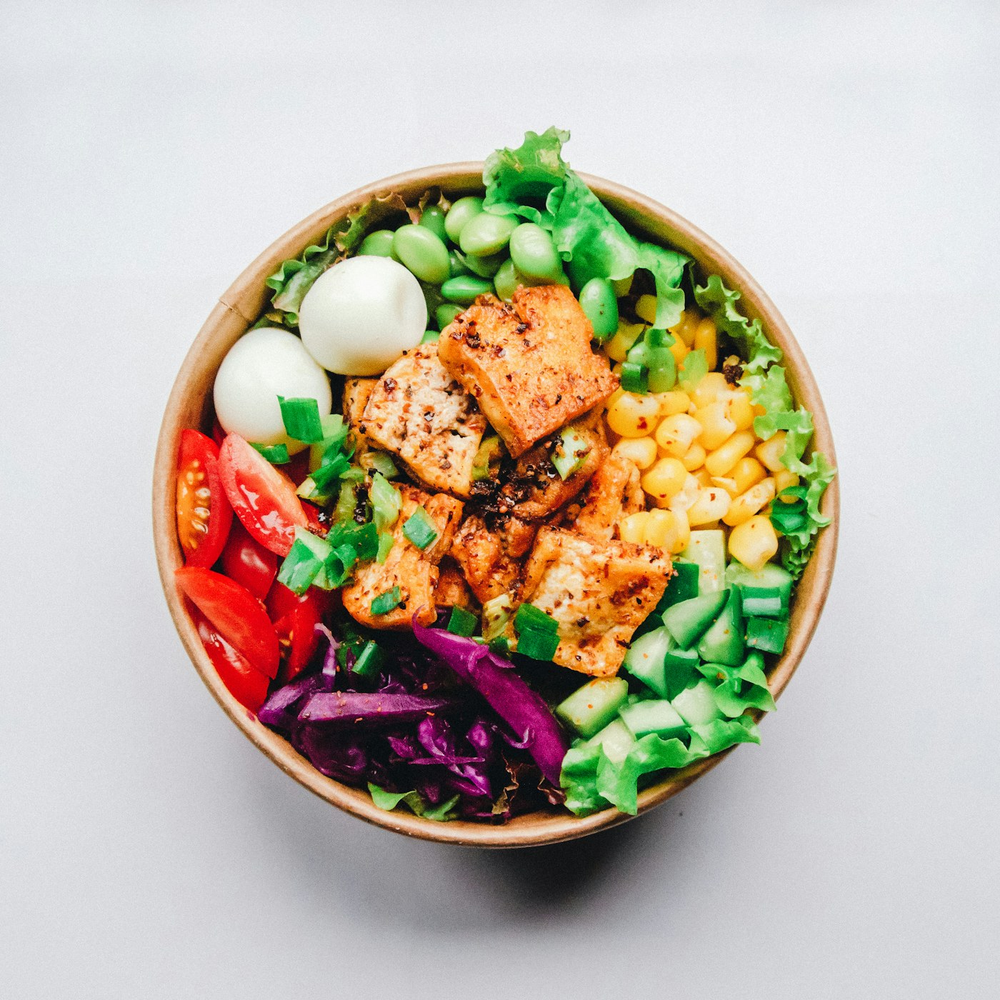 A colorful, fully prepared takeaway meal of greens, roasted protein, corn and tomatoes, ready to share