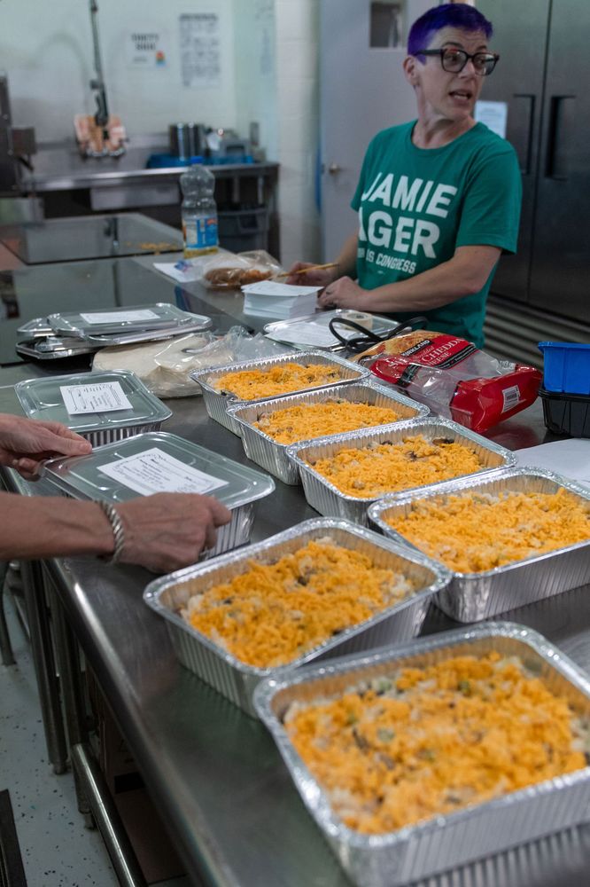 A volunteer smiling behind a counter lined with prepared trays